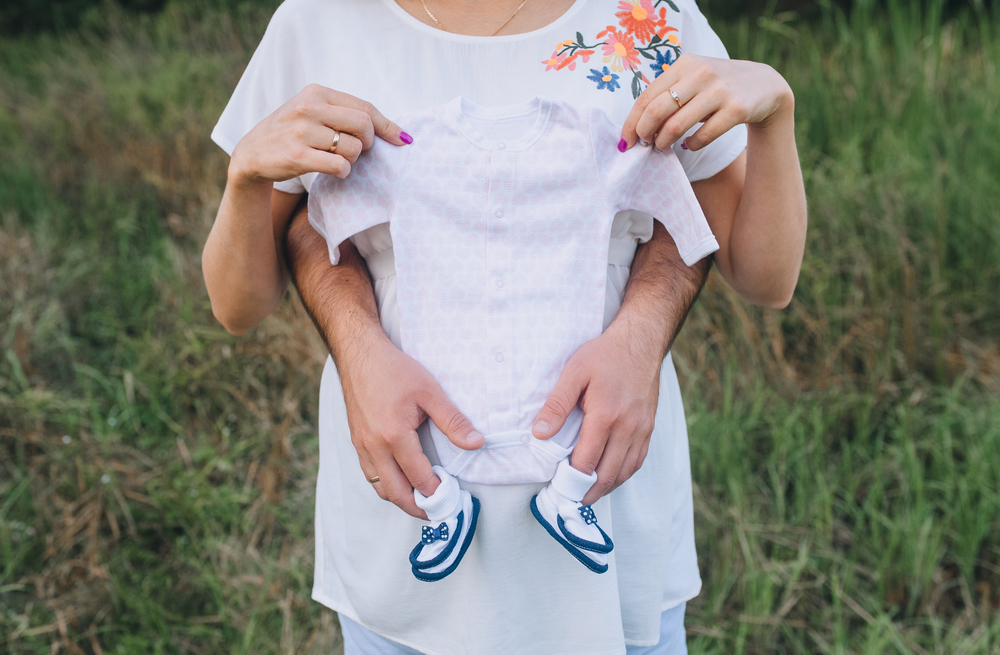  man and a pregnant woman holding baby clothes for a newborn