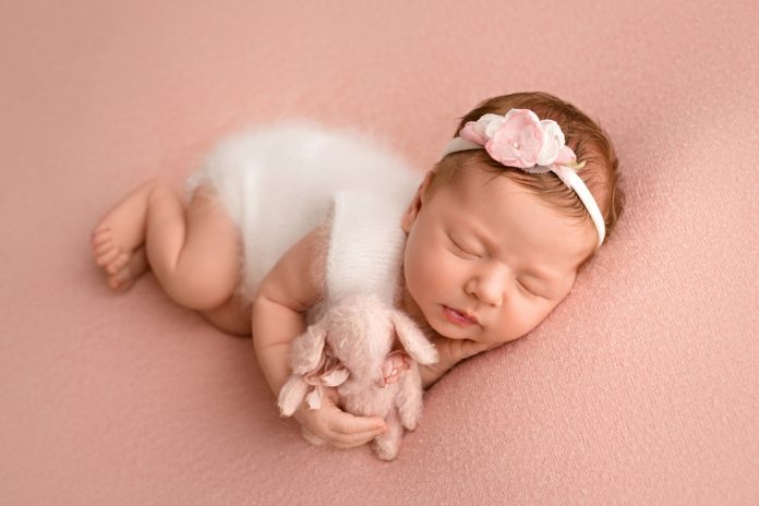 newborn baby girl sleeping in a white jumpsuit with pink rabbit