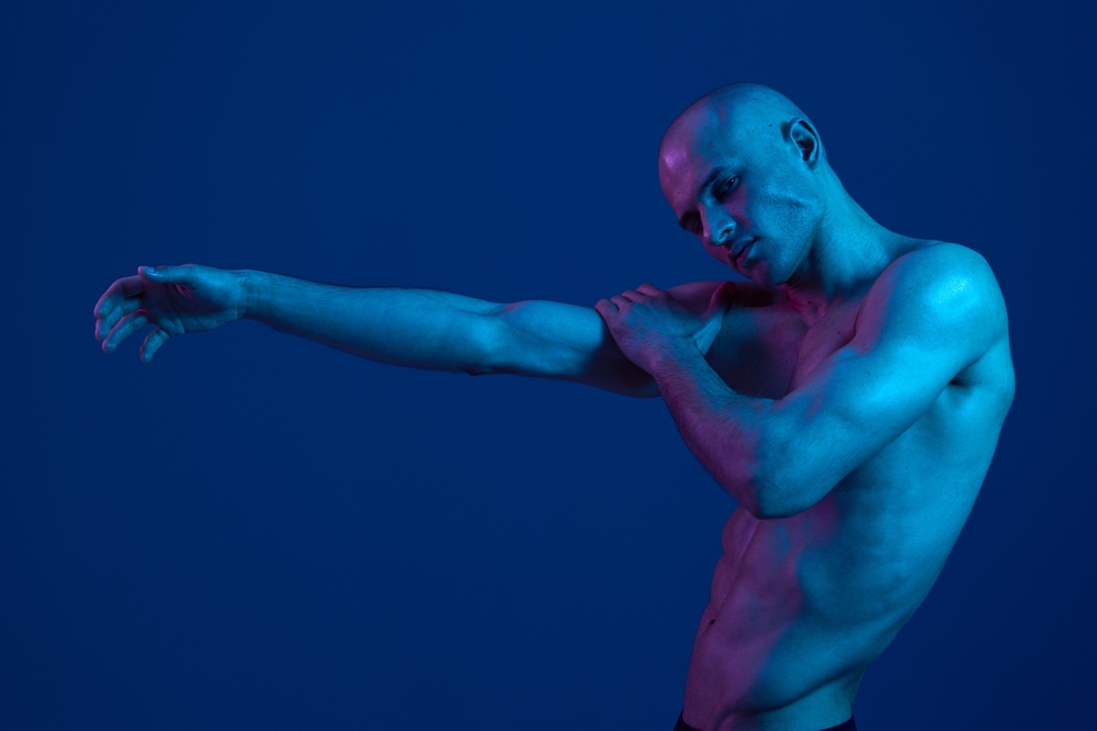 Nude man with arm outstretched lit with blue light