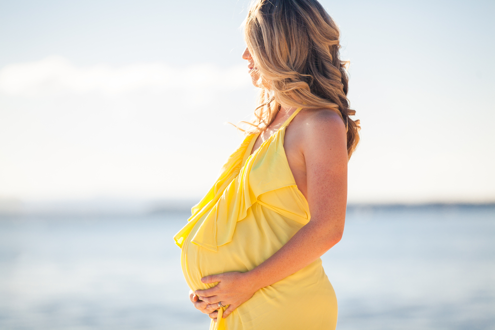 Profile of a pregnant woman in yellow dress on the beach